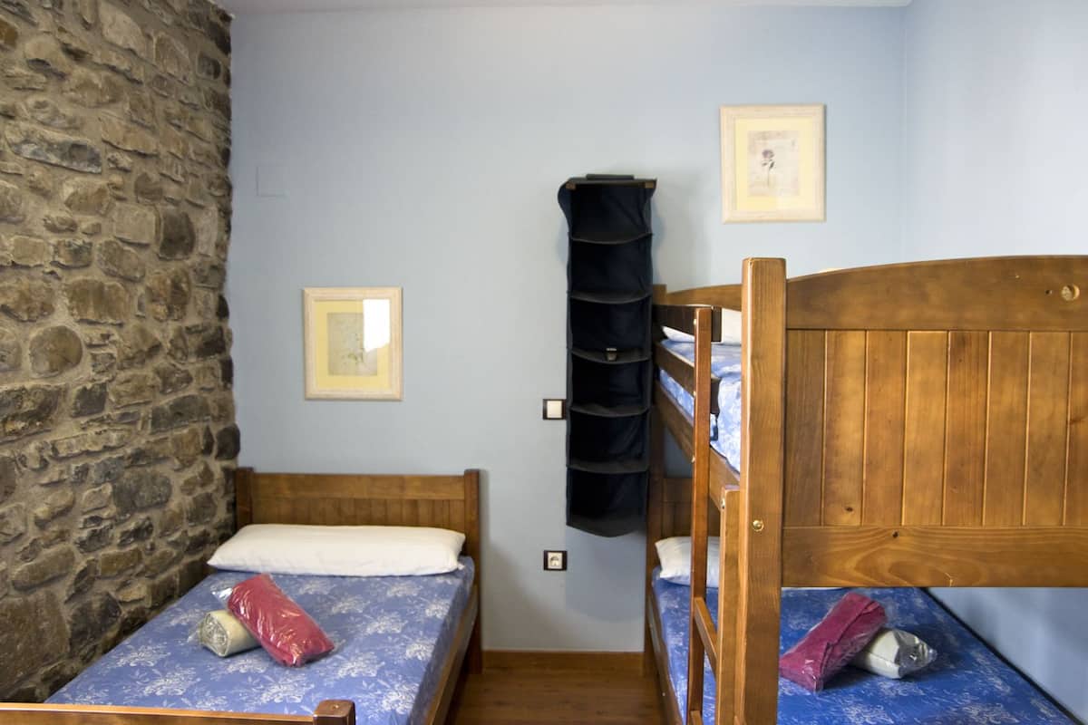 A room with two bunk beds, a stone wall, and a shelf with folded clothes.