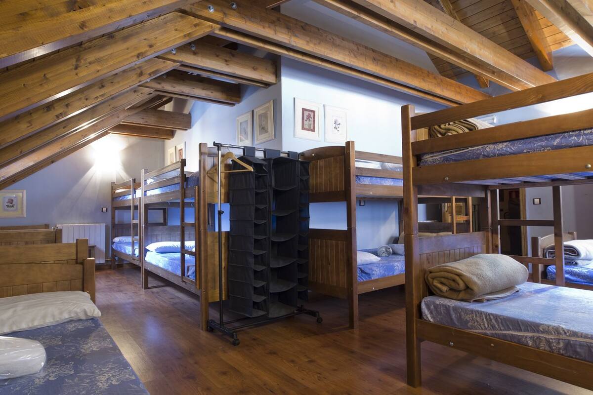 A dormitory-style room with bunk beds, wooden beams, and a radiator.