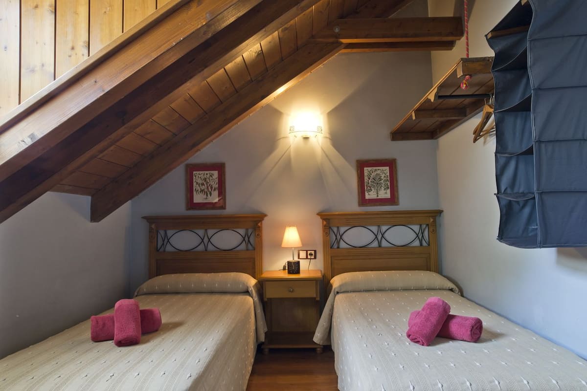 A cozy attic bedroom with two beds, wooden beams, and a sloped ceiling.