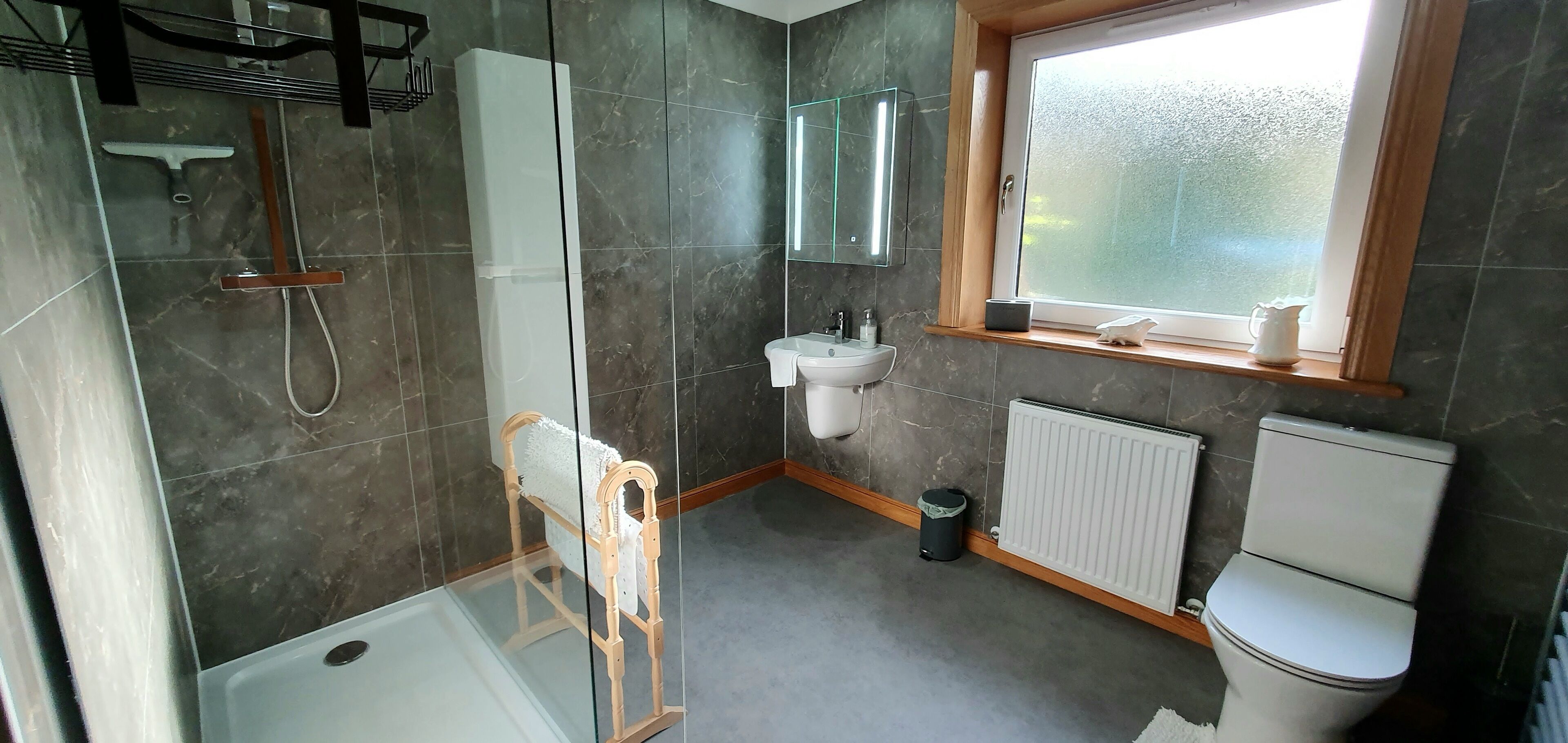 A modern bathroom with a shower, toilet, sink, and a window.