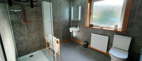 A modern bathroom with a shower, toilet, sink, and a window.