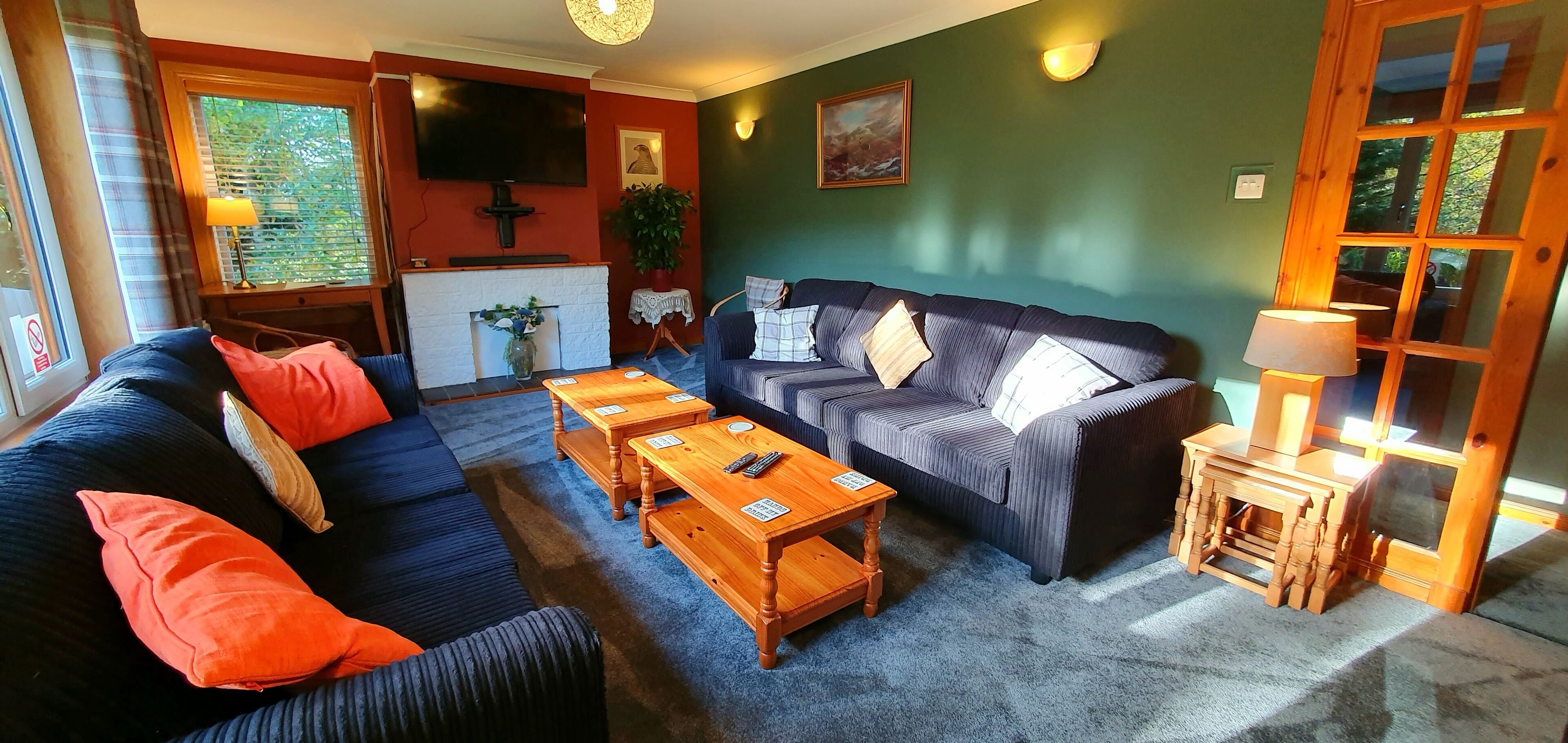 A cozy living room with a dark blue sofa, orange cushions, a wooden coffee table, and a television mounted on the wall.