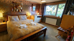 A bedroom with a bed, bedside tables, a dresser, a mirror, and a window with curtains. - Torcroft Lodges (Inverness)