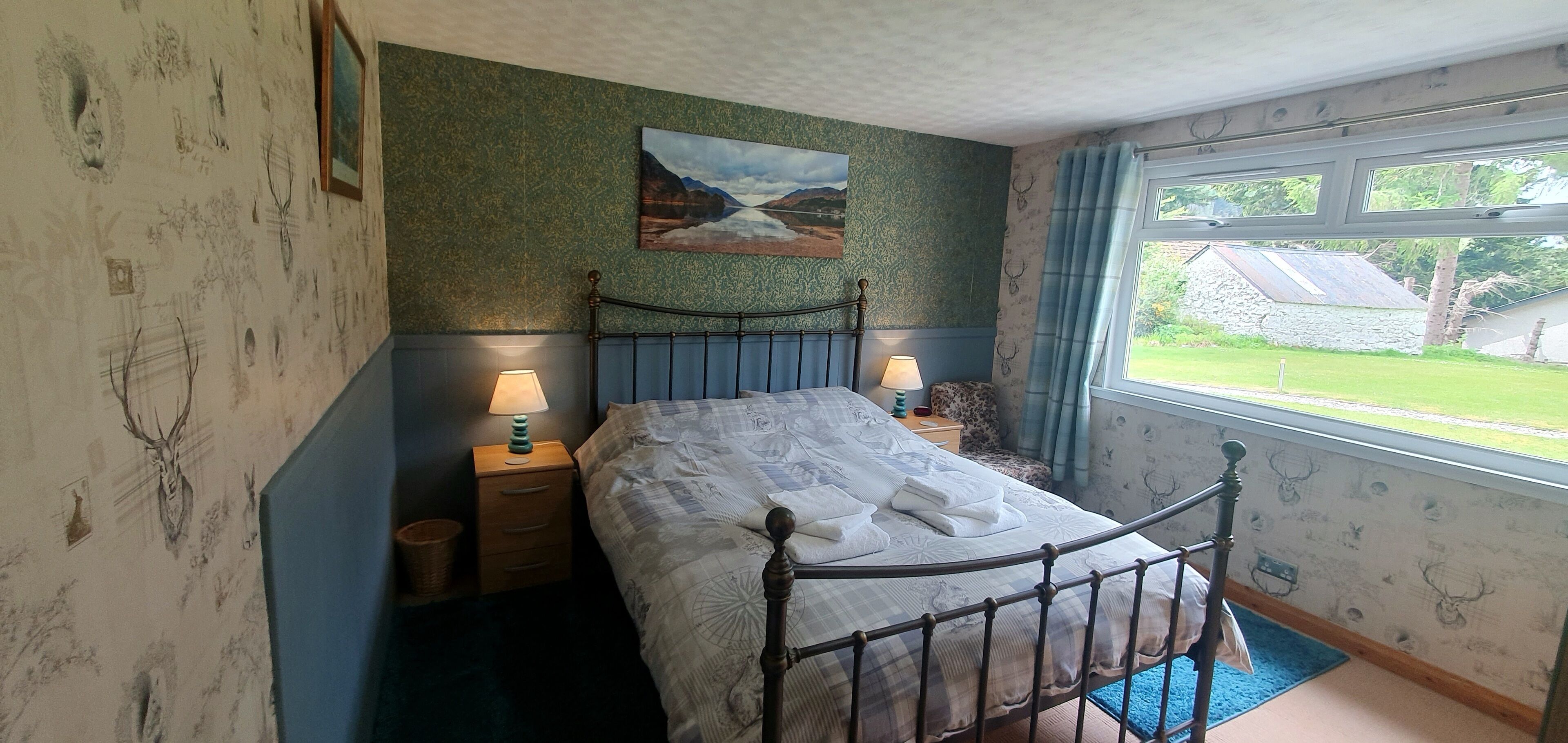 A bedroom with a bed, two bedside tables with lamps, a window with curtains, and a painting on the wall.