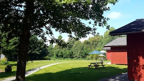 A red building with a picnic table and umbrella, surrounded by a well-maintained lawn and trees. - Torcroft Lodges (Inverness)