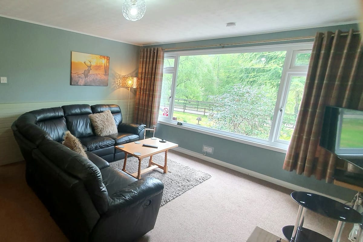 A living room with a black leather sofa, a wooden coffee table, and a TV on a stand.
