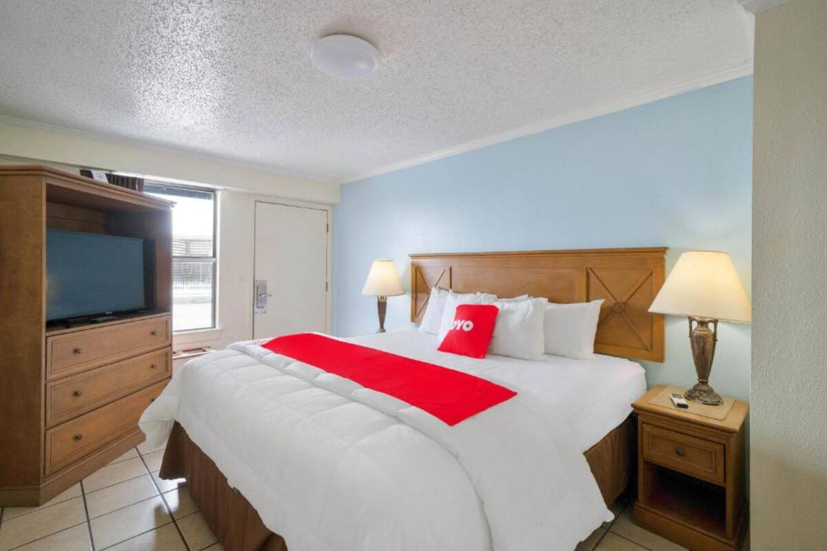 Habitación de hotel con una cama, dos lámparas de noche, un televisor, un aparador de madera y una ventana.