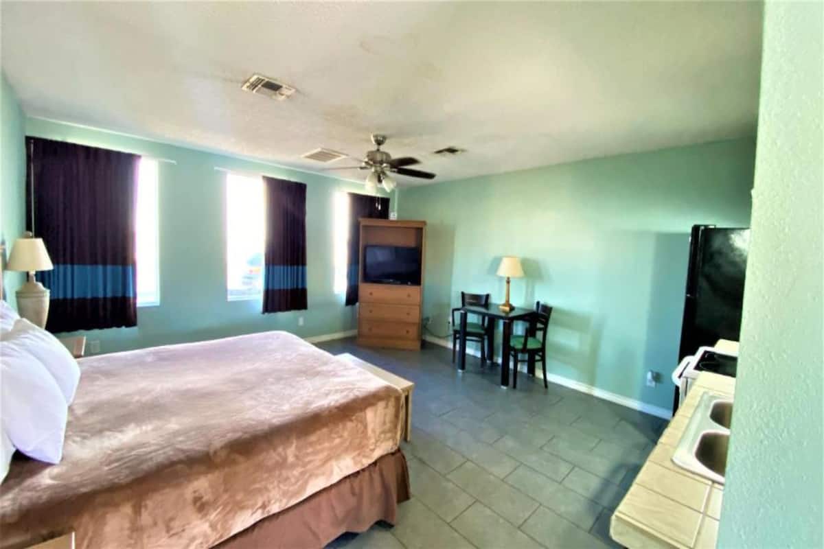 Habitación de hotel con cama, escritorio, silla, televisión y baño con lavamanos y espejo.