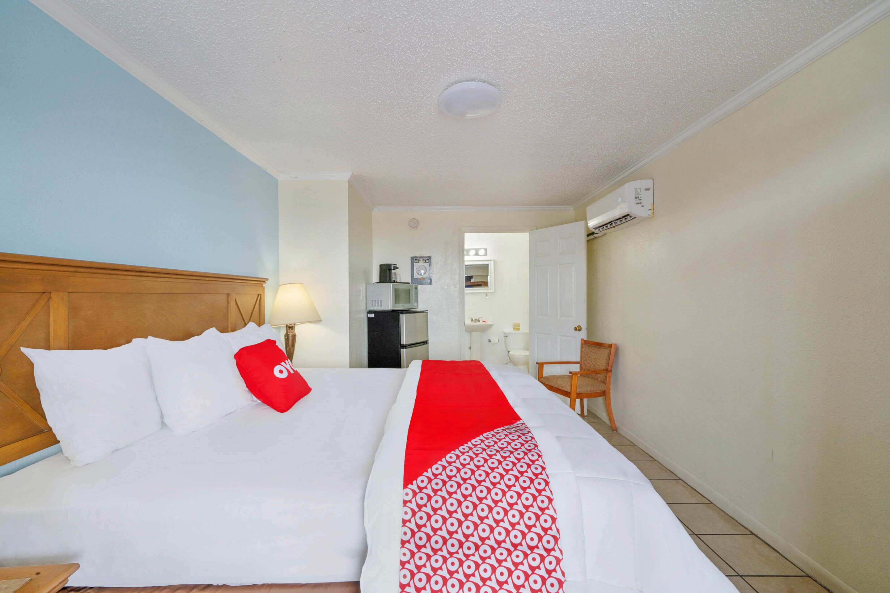 Una camera d'albergo con un letto, una scrivania, una sedia, una lampada e un condizionatore d'aria.