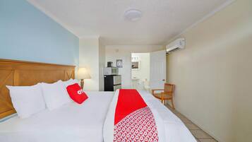 Una camera d'albergo con un letto, una scrivania, una sedia, una lampada e un condizionatore d'aria.