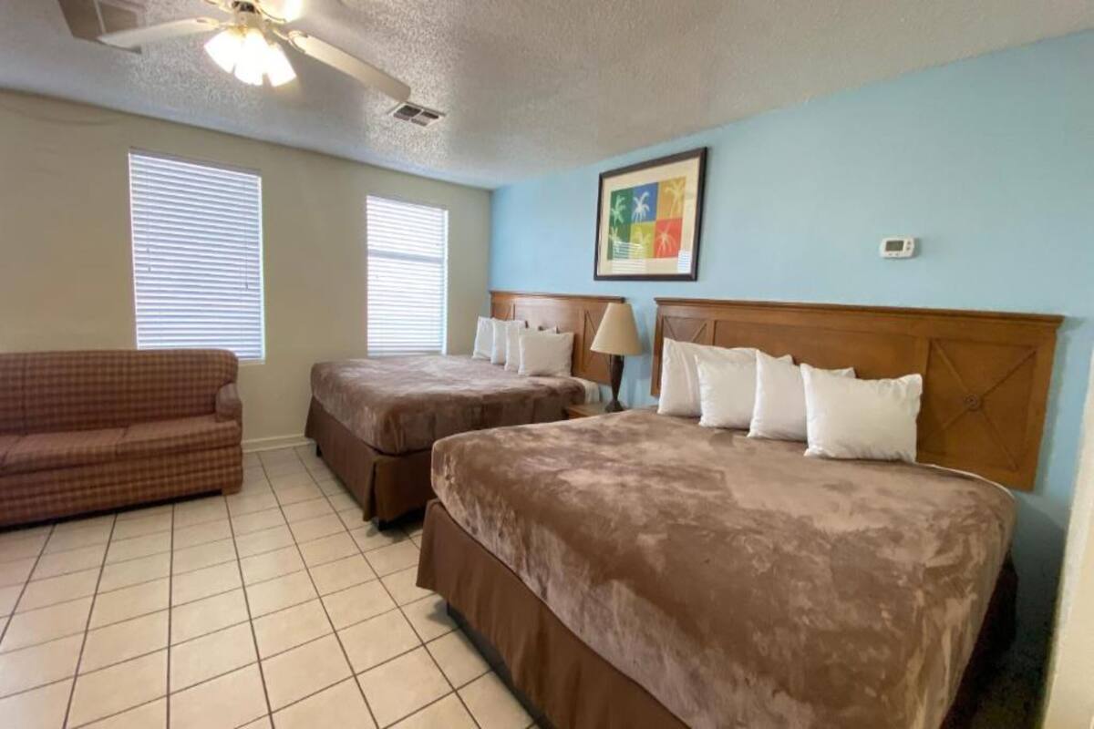Habitación de hotel con dos camas, un sofá y un ventilador de techo.