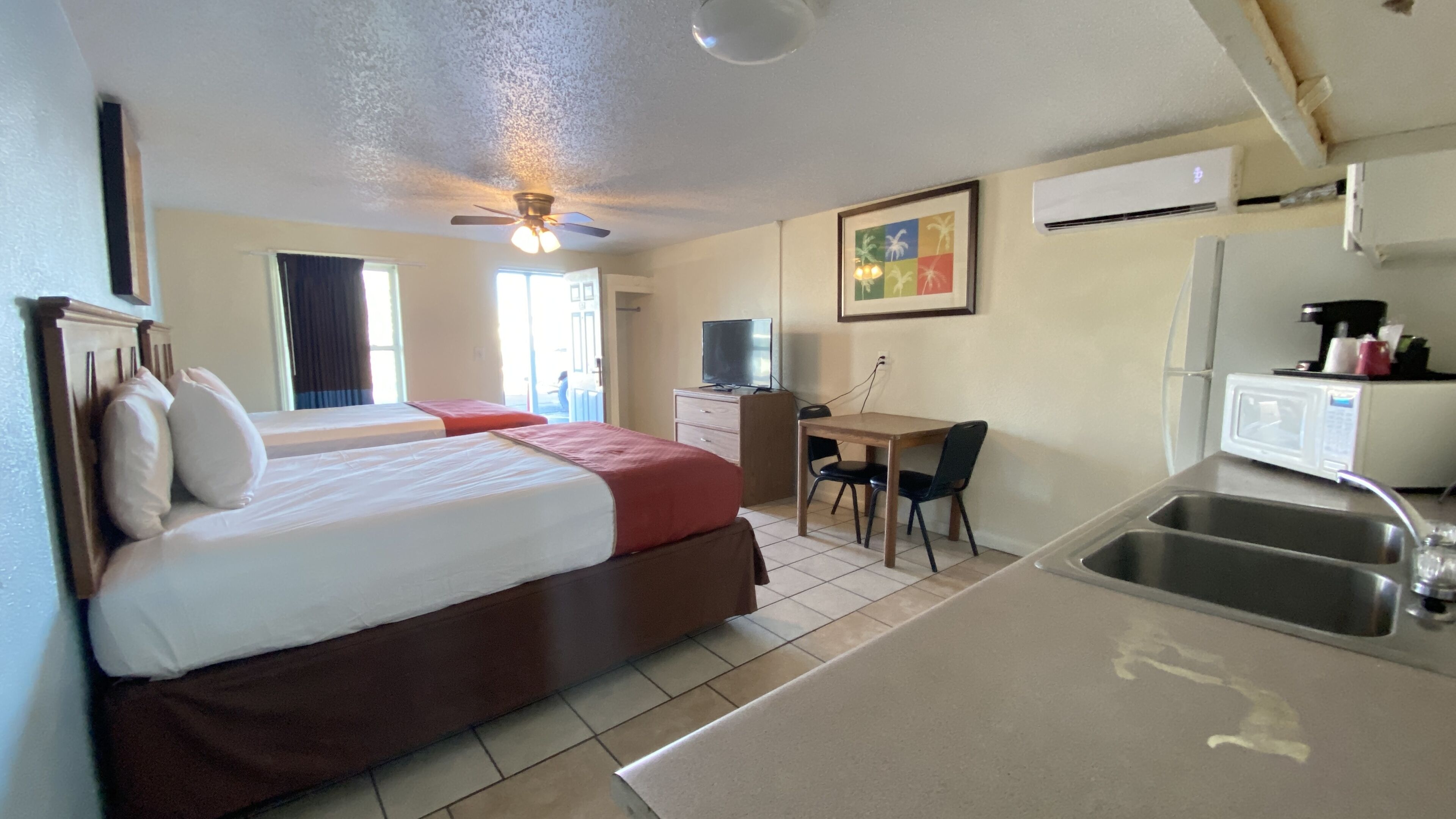 Habitación de hotel con cama, escritorio, silla, microondas y lavamanos.