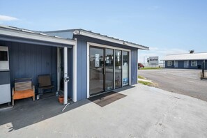 Een klein gebouw met een deur, ramen, een bankje en een mat voor de deur.