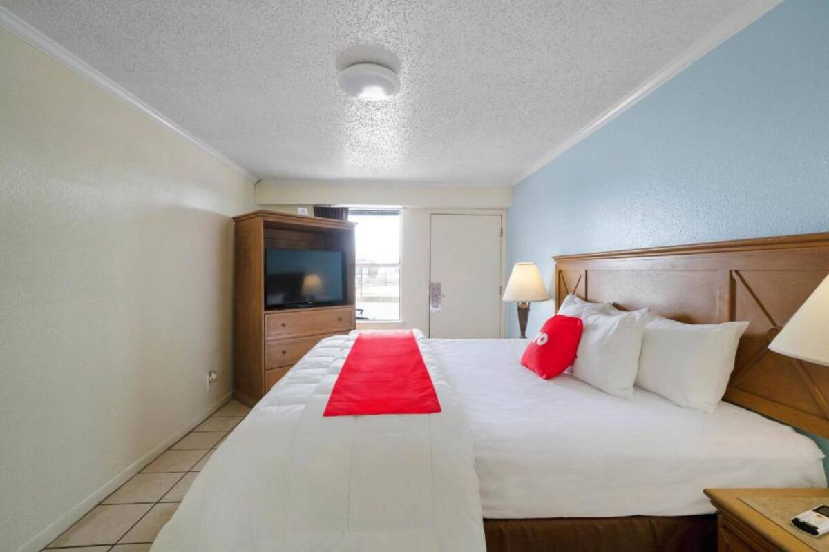 Habitación de hotel con una cama, televisión, lámpara y cabecera de madera.