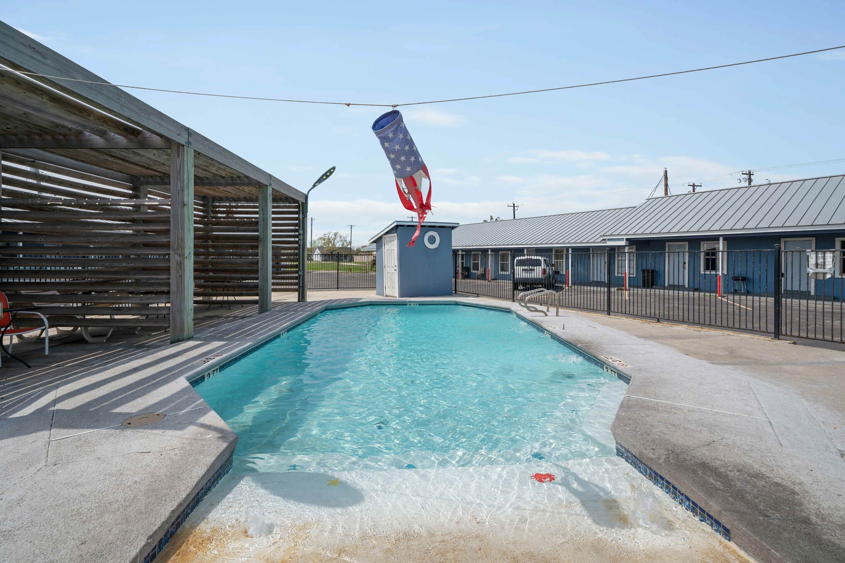 Une piscine dotée d’une zone couverte et d’un petit bâtiment avec une fenêtre circulaire.