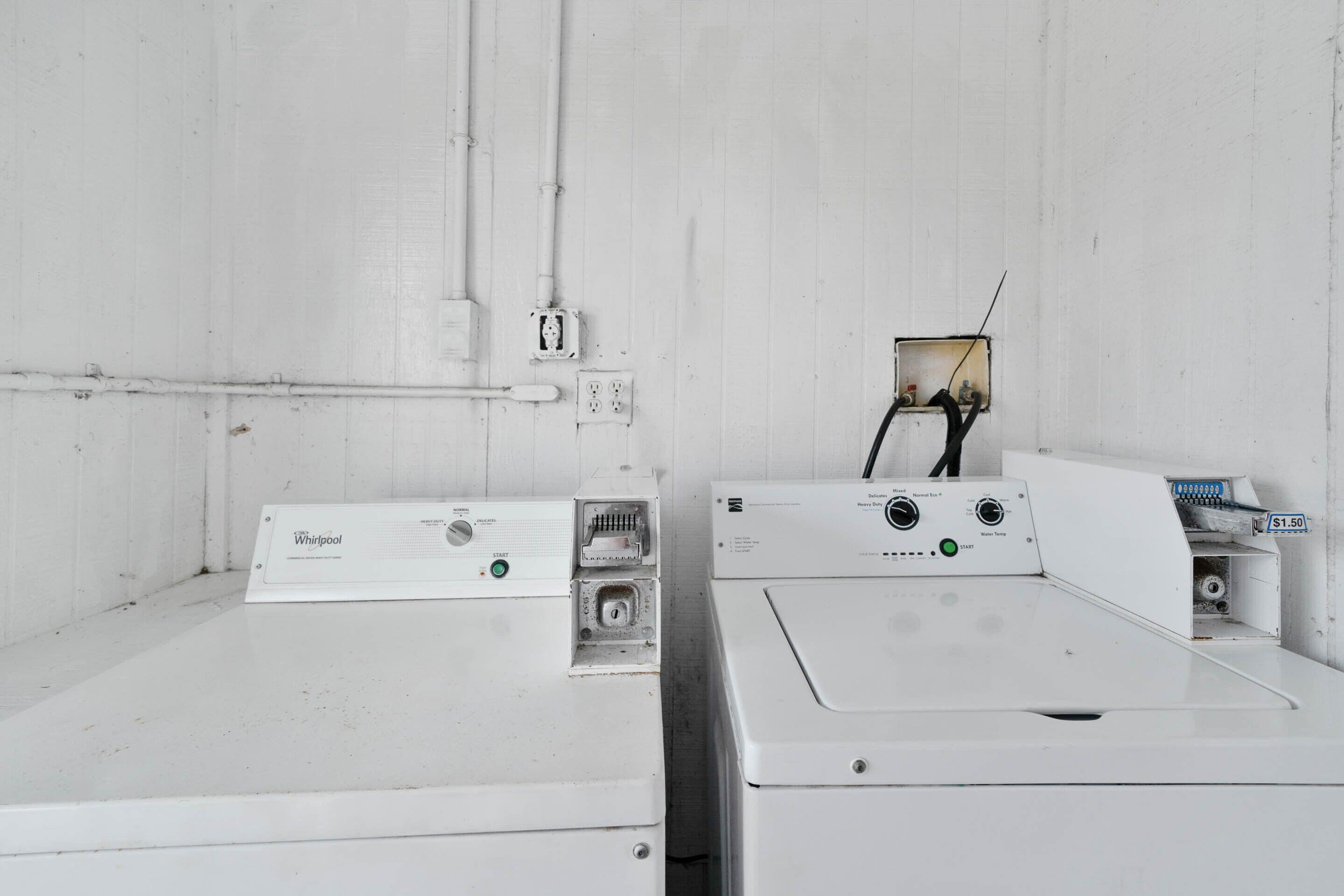 Two white Whirlpool washers in a room with white walls and a visible electrical outlet.
