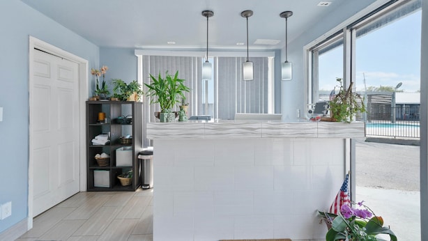 Una cocina moderna con una isla blanca, luces colgantes y vistas al exterior.