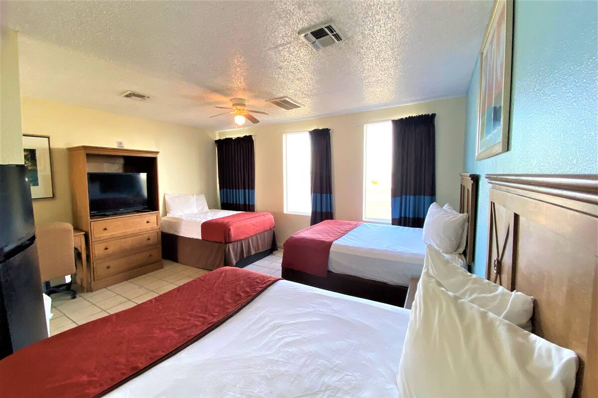 Habitación de hotel con dos camas, un escritorio, un televisor y un ventilador de techo.