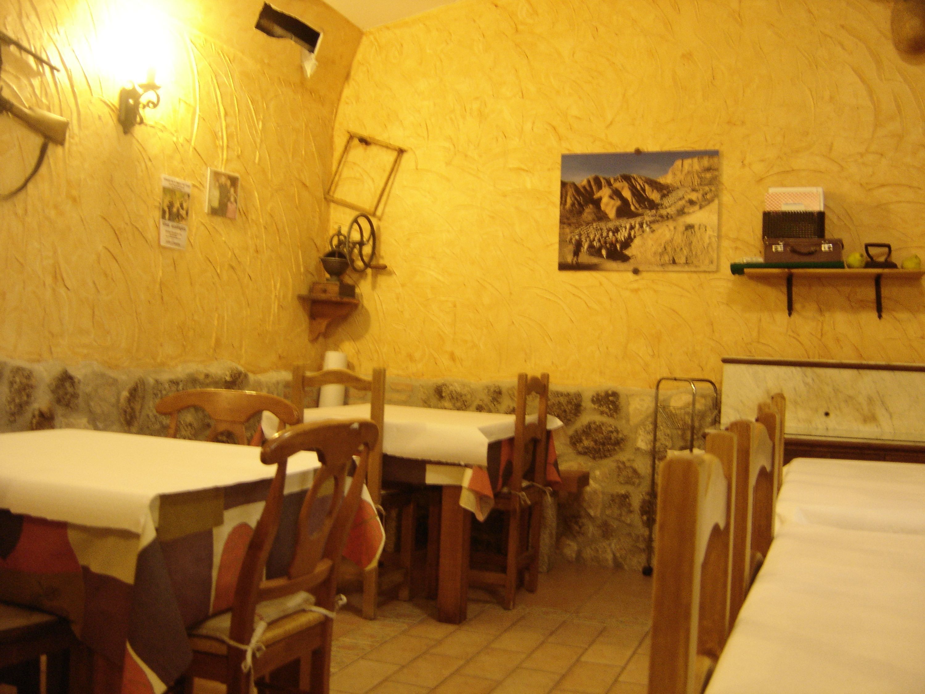 A dining area with wooden tables and chairs, a stone wall, and a painting of a mountainous landscape.