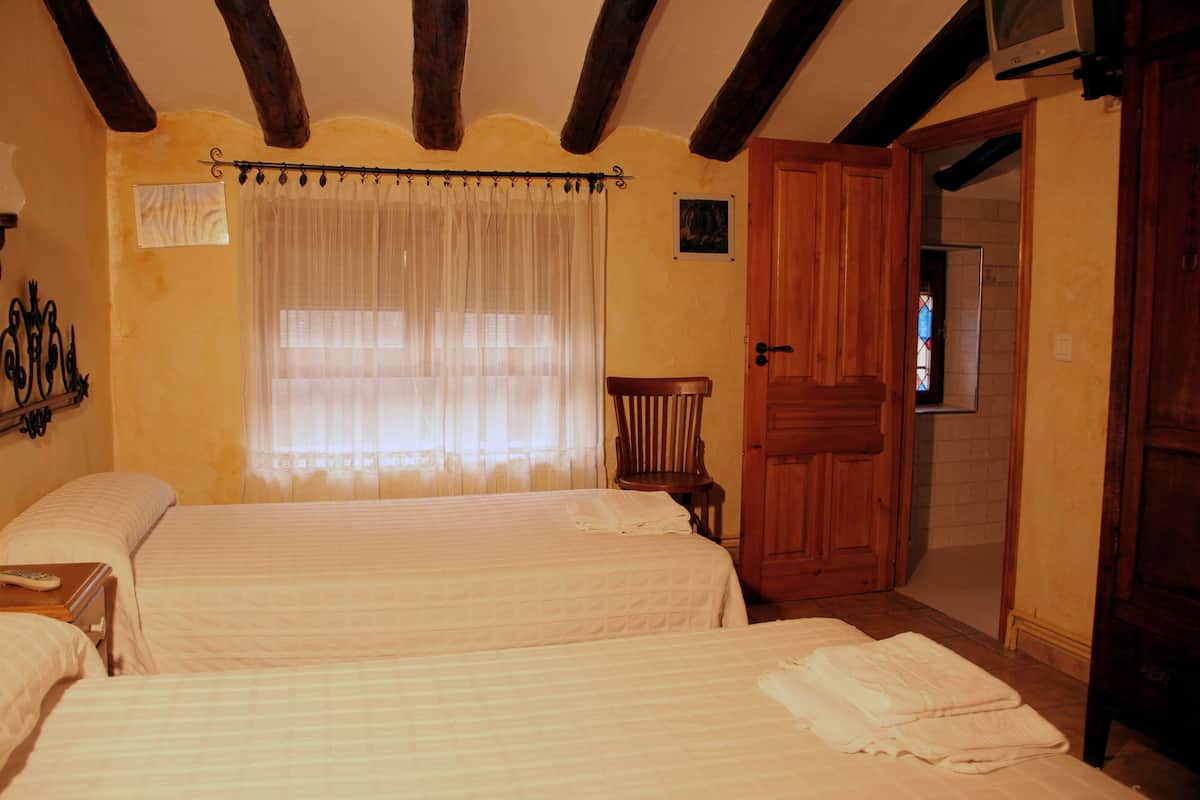 Una habitación con dos camas, una puerta de madera, una silla y un televisor en la pared.