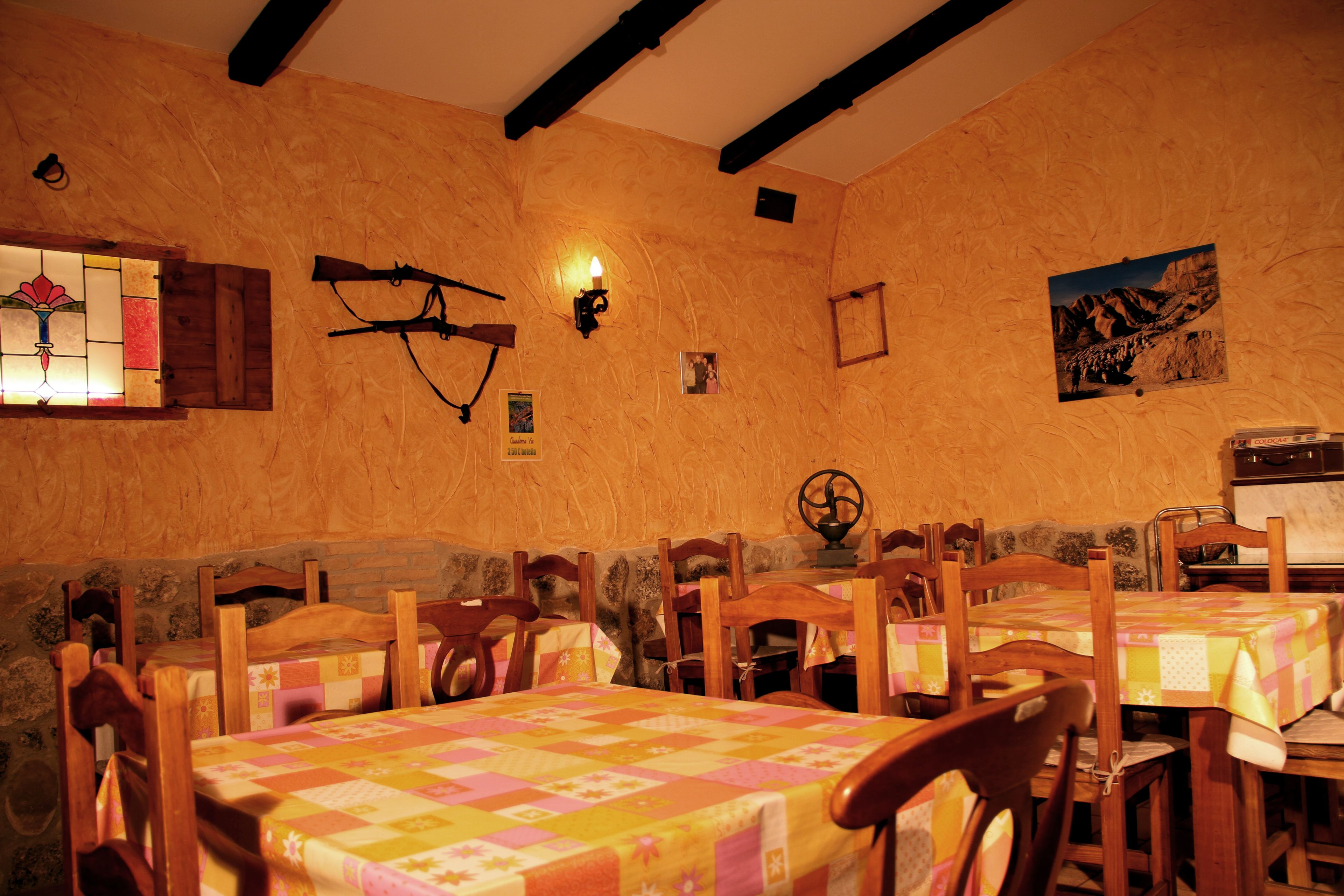 Un rincón comedor acogedor con mesas y sillas de madera, una ventana con vidrieras de colores y un aplique de pared.