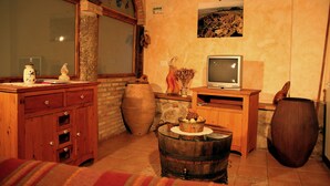 A rustic room with a wooden cabinet, a television on a wooden stand, a large vase, and a stone wall. - Casa rural La Bardena Blanca I (Arguedas)