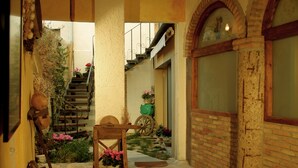 A courtyard with a wooden bench, potted plants, a rustic wooden door, and a brick wall. - Casa rural La Bardena Blanca I (Arguedas)
