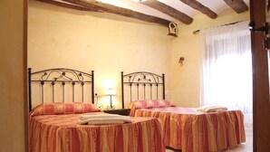 A room with two beds, each with a striped bedspread, a nightstand with a lamp, and a window with sheer curtains. - Casa rural La Bardena Blanca I (Arguedas)