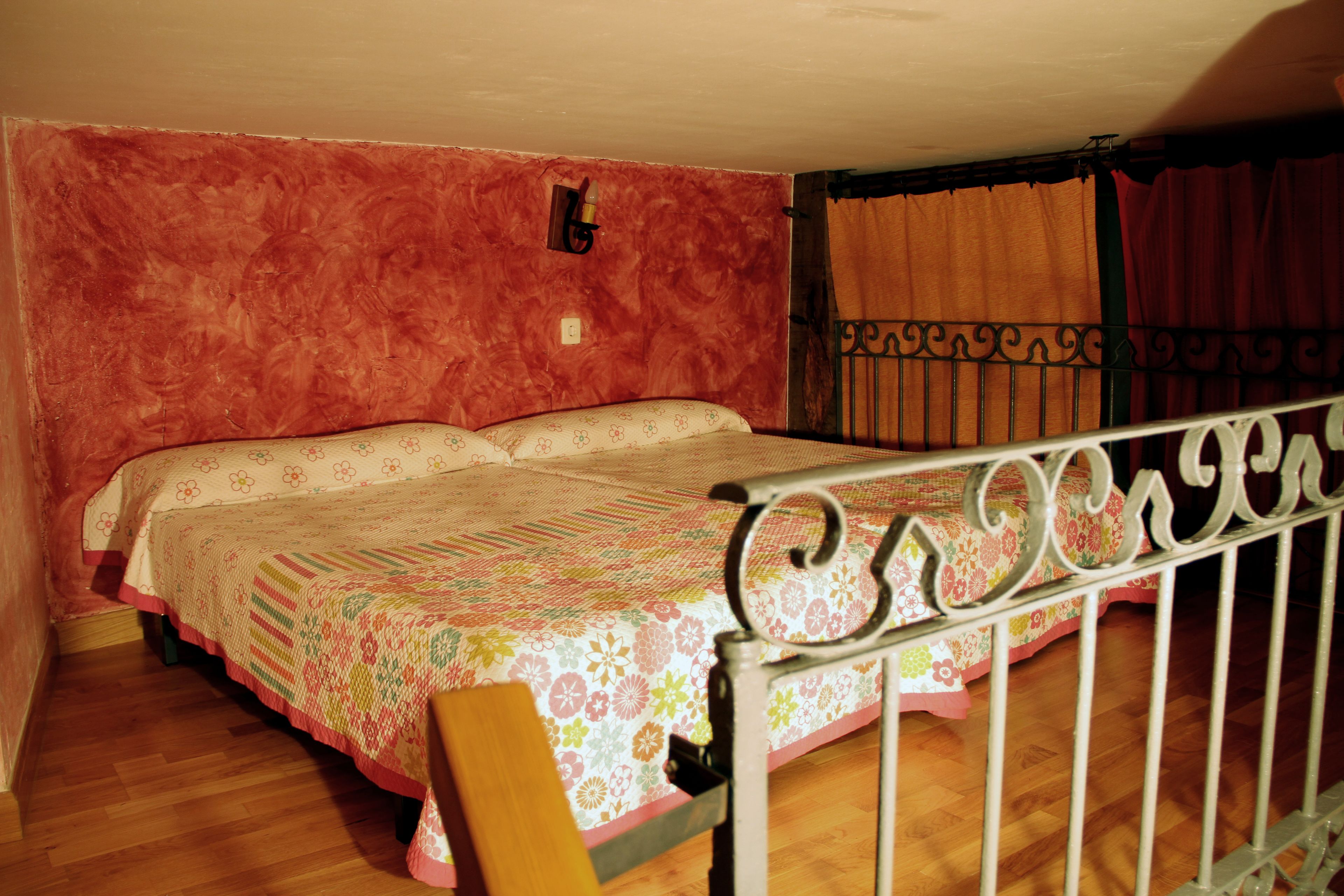 Quarto com uma cama, uma cadeira de madeira, estrutura de cama de metal, uma luminária na parede e uma cortina.