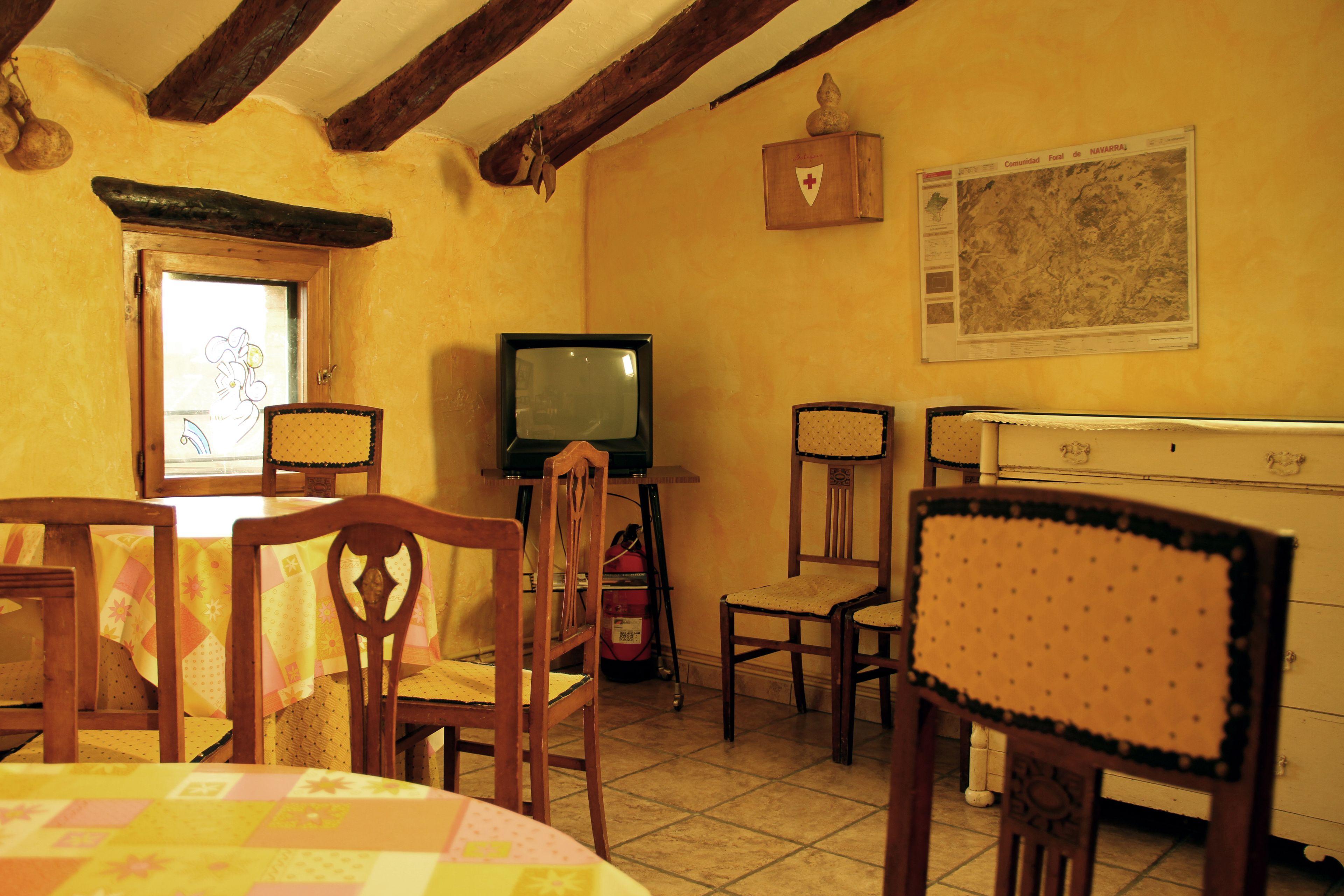 A dining area with wooden chairs, a table with a quilt, a television, and a map on the wall.