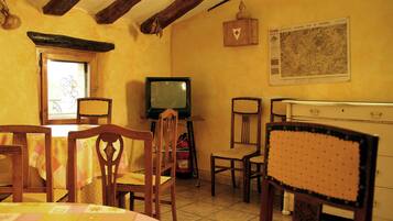 A dining area with wooden chairs, a table with a quilt, a television, and a map on the wall.