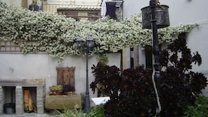 A narrow street with white flowering vines on a building, a stone bench, and a metal lamp post. - Casa rural La Bardena Blanca I (Arguedas)