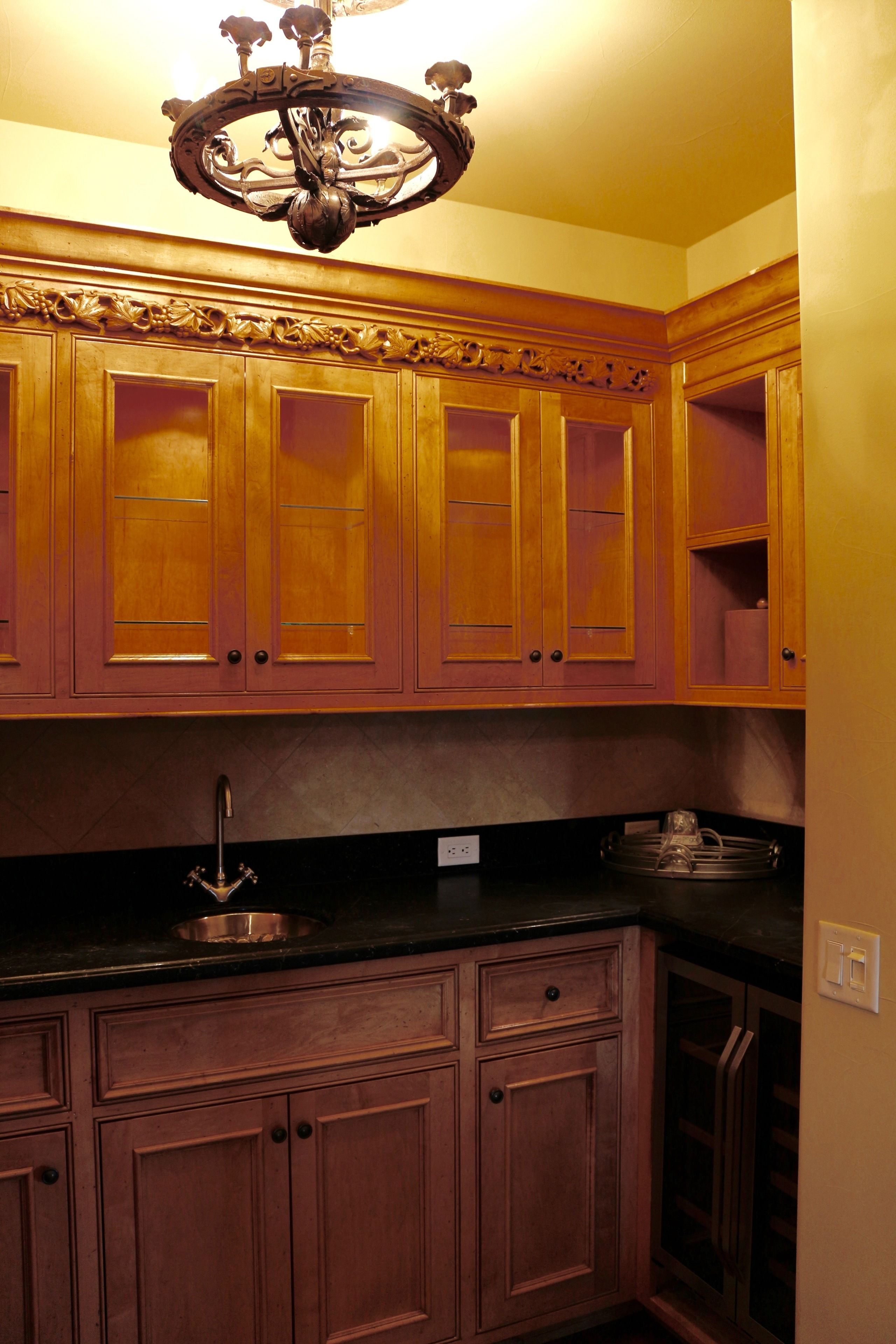 A kitchen with wooden cabinets, a black countertop, and a chandelier.
