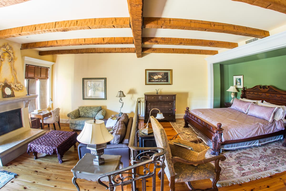Une pièce chaleureuse avec une cheminée, un canapé, un lit et des poutres en bois au plafond.