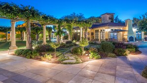 Un espacio exterior bien iluminado con una pérgola, un sendero de piedra y abundante jardinería.