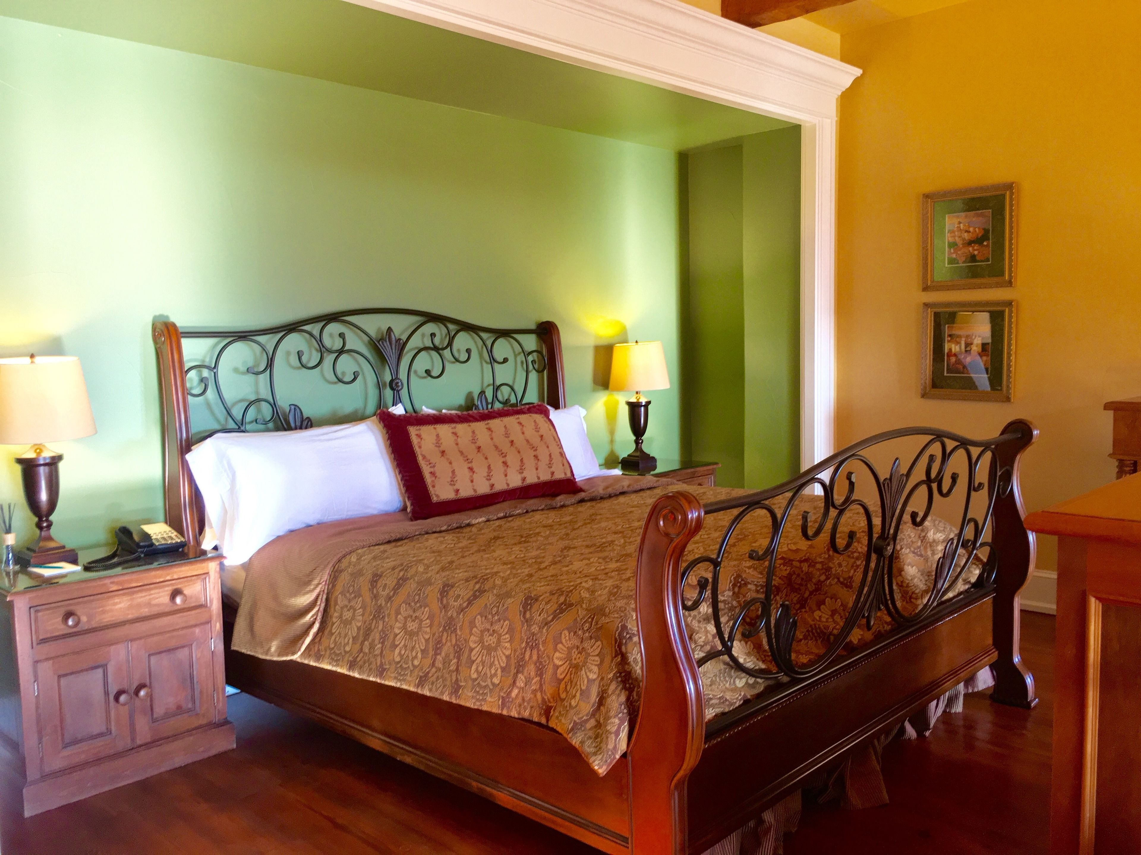 A neatly made bed with a wooden headboard, two bedside tables with lamps, and a green wall.