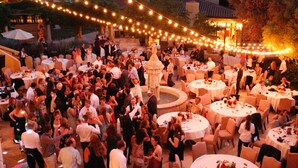 Un evento al aire libre con mesas redondas e iluminacion con luces colgantes.