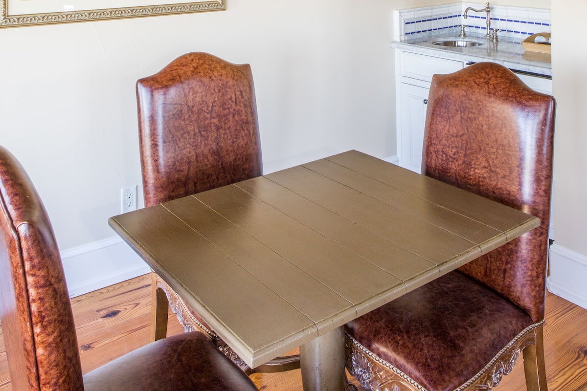 Un coin repas avec une table et quatre chaises, une cuisine avec des meubles blancs et deux tableaux encadrés au mur.