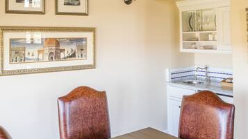 Uma sala de jantar com uma mesa e quatro cadeiras, uma cozinha com armários brancos e duas imagens emolduradas na parede.