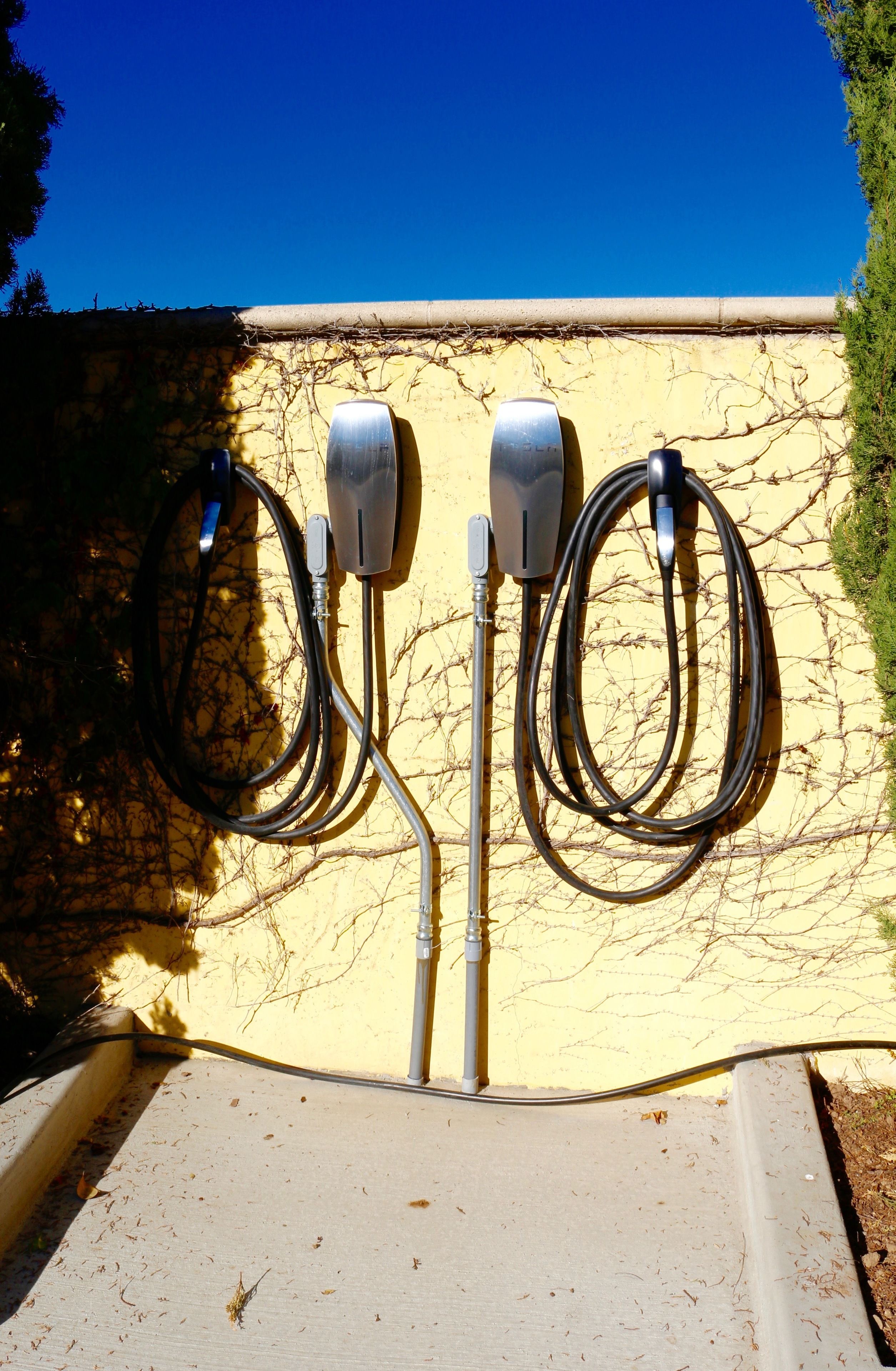 Two outdoor electrical outlets mounted on a wall with a clear blue sky in the background.