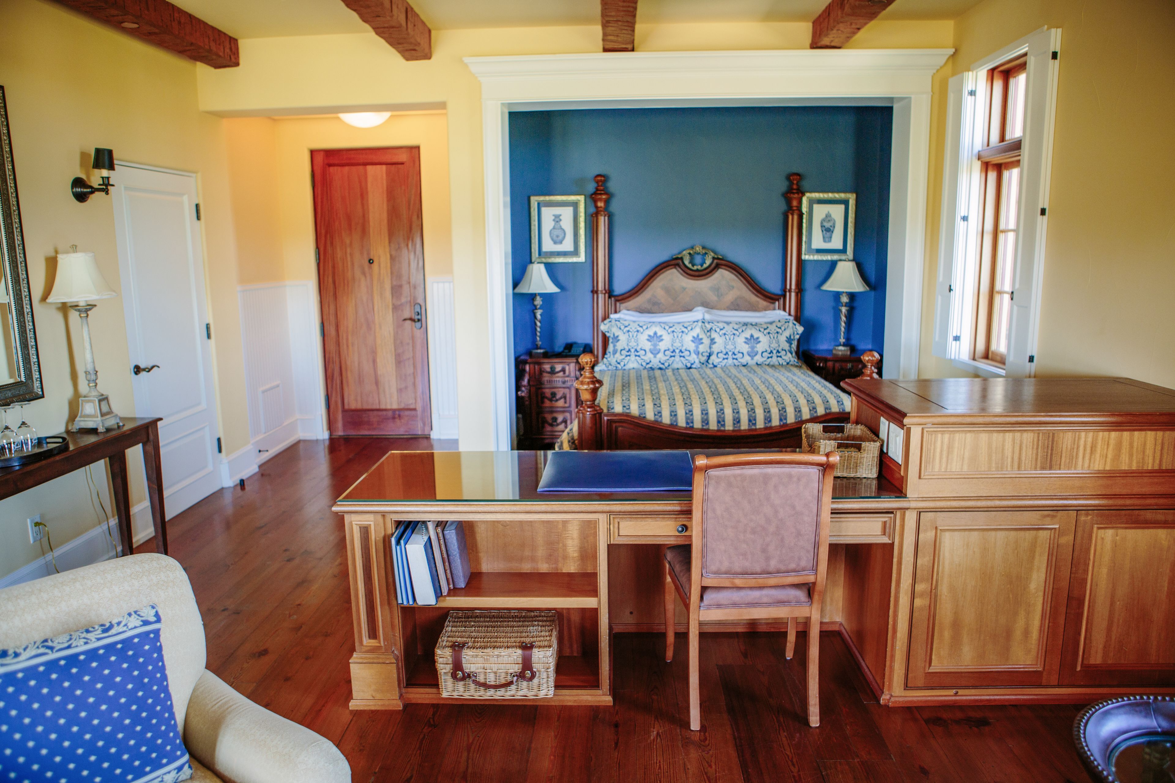 A bedroom with a wooden bed, a desk, and a chair. There is a door leading to another room.
