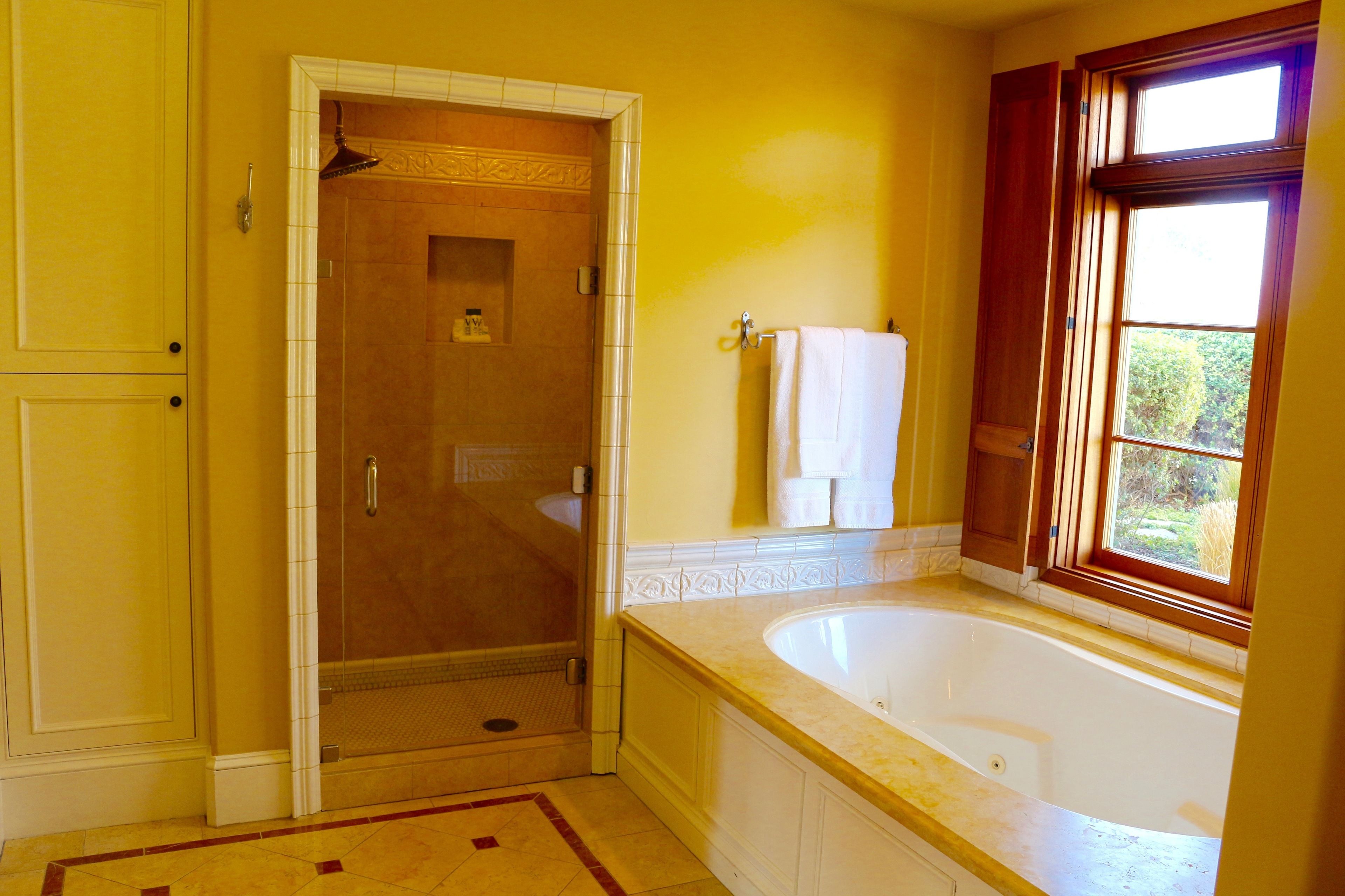 A bathroom with a walk-in shower, a bathtub, and a window with curtains.