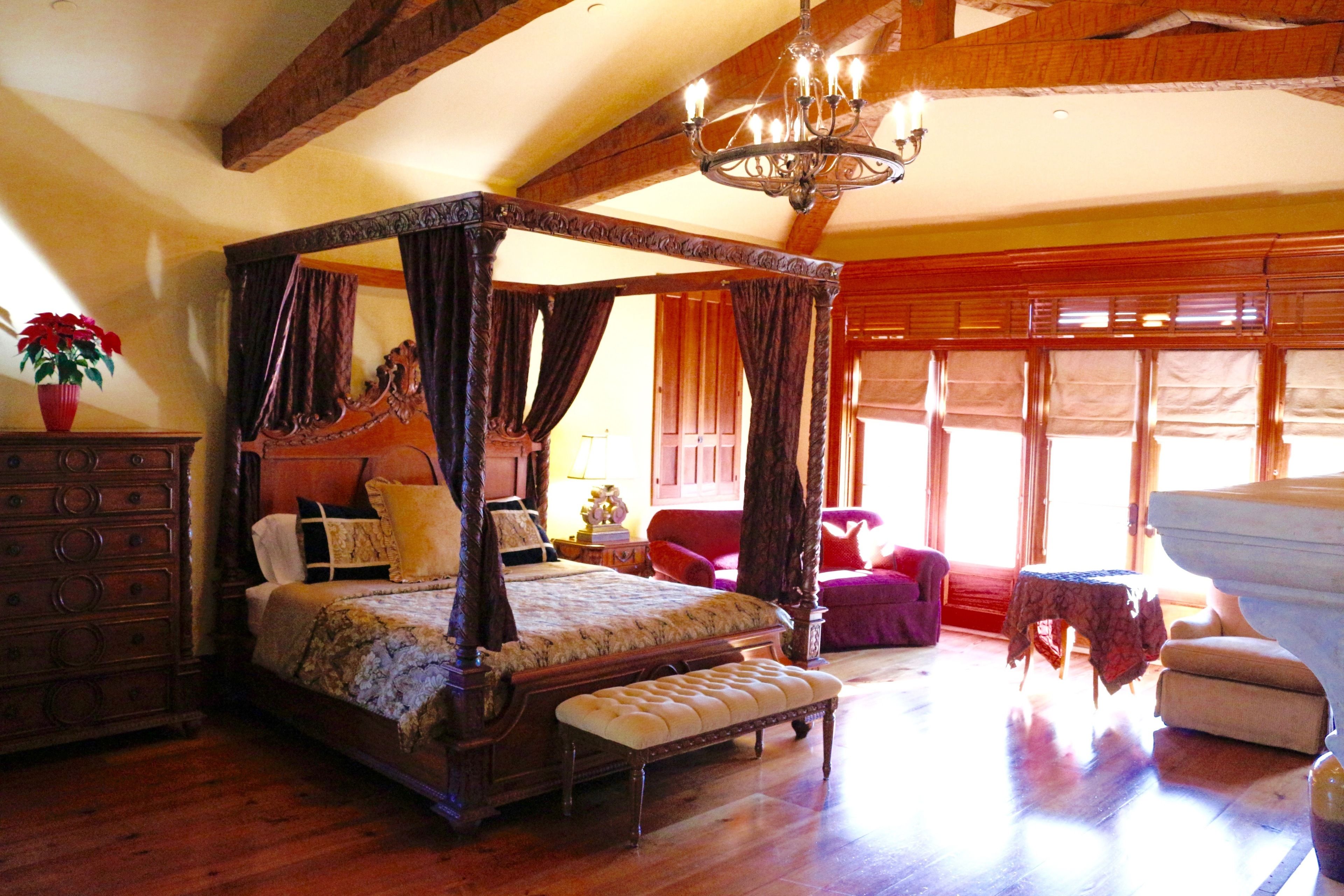 A four-poster bed with a canopy, wooden floor, and a chandelier.