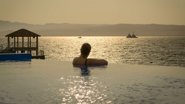 A person in a swimming pool with a dock and a boat in the background. - Apartamento Frente Islas Ballestas (Paracas)