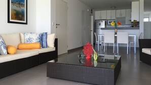 A modern living room with a sofa, a coffee table with decorative items, a dining area with chairs, and a kitchen in the background. - Apartamento Frente Islas Ballestas (Paracas)
