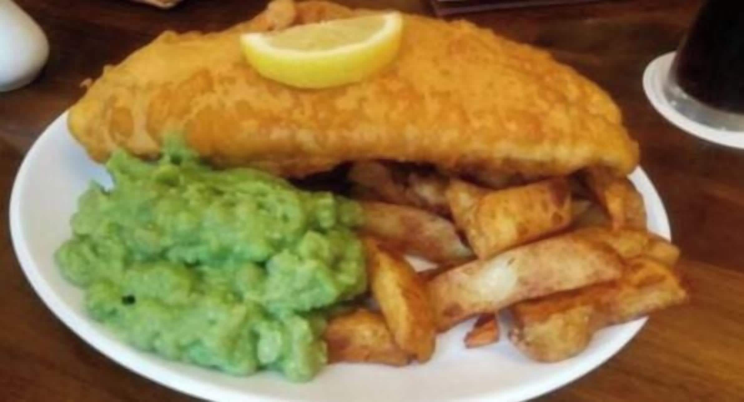 A plate with fish and chips, a slice of lemon, and a portion of mushy peas.