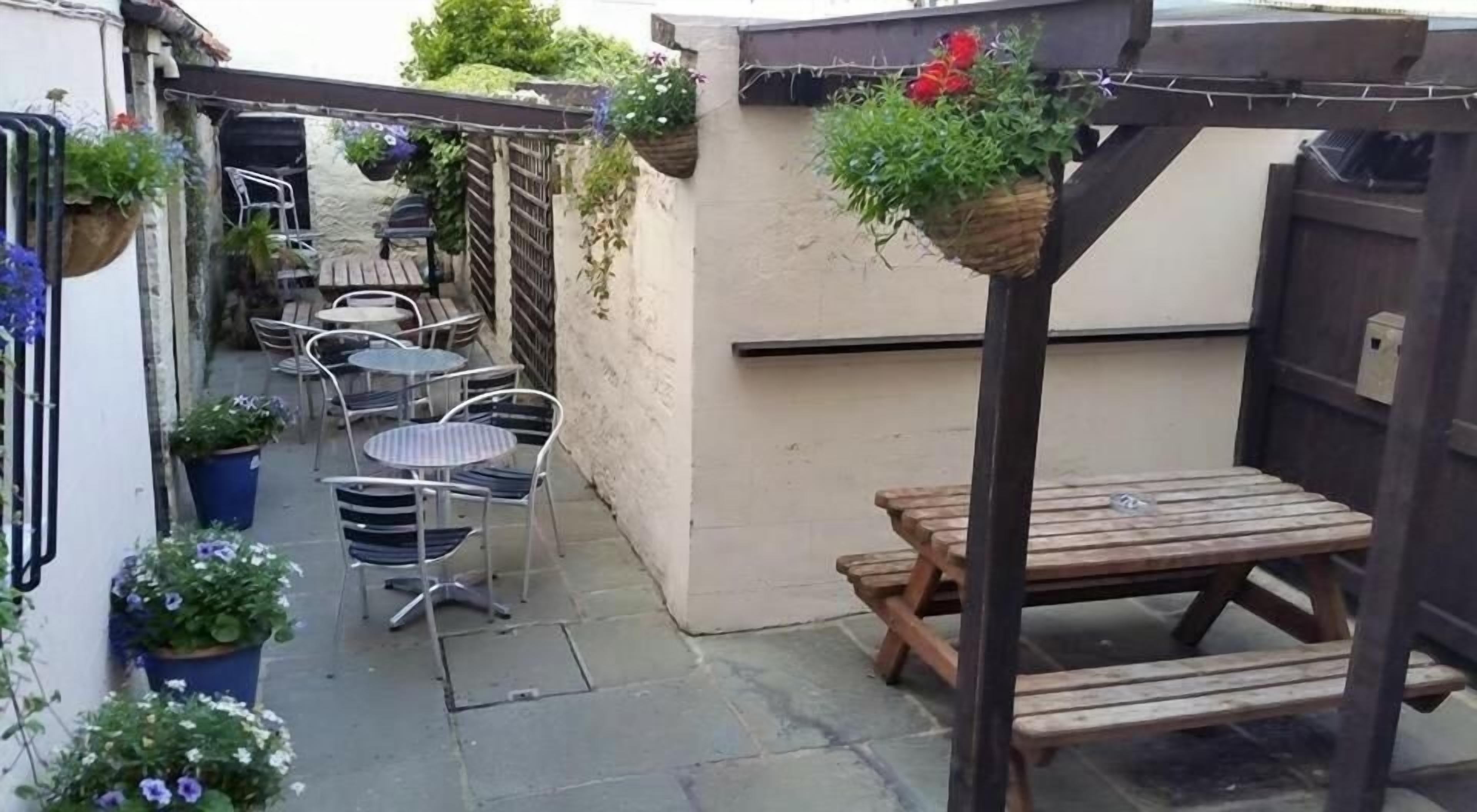 En terrasse med udendørs møbler, blandt andet et bord og stole, samt krukker med planter.