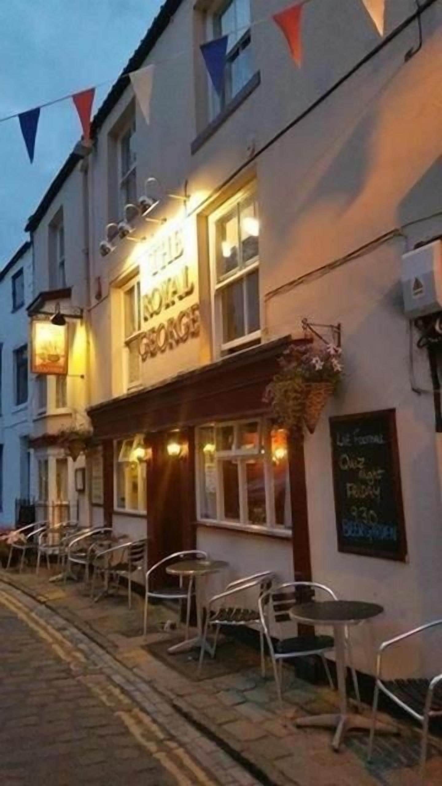A pub named 'The Royal George' with outdoor seating and a signboard displaying prices.