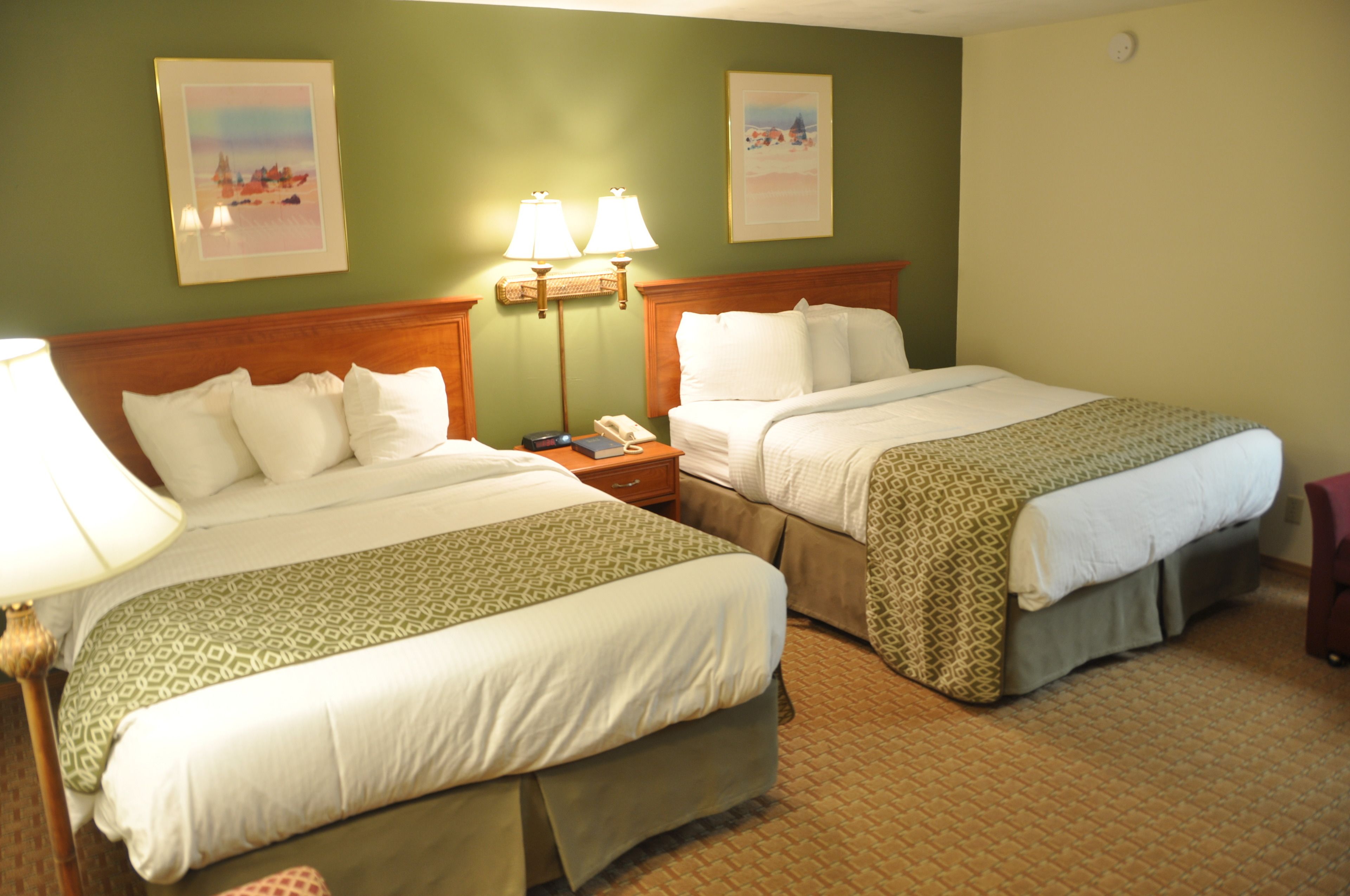 A hotel room with two beds, a nightstand with a phone and lamp, and two framed pictures on the wall.