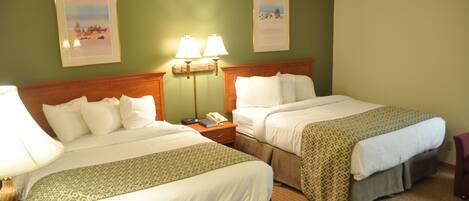 A hotel room with two beds, a nightstand with a phone and lamp, and two framed pictures on the wall.